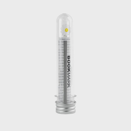 Clear cylindrical shaped container with white daisy flower metal bookmark inside.