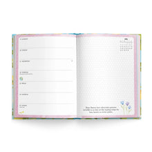 An open planner or weekly layout book showing two interior pages with a pastel floral cover. The left page has weekly time slots from Monday to Sunday, and the right page has a blank grid with a small April calendar and decorative text near the bottom.