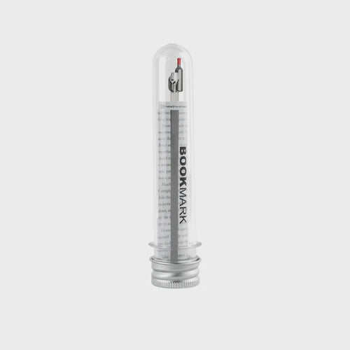 Clear cylindrical container with a wine bottle shaped metal bookmark inside.