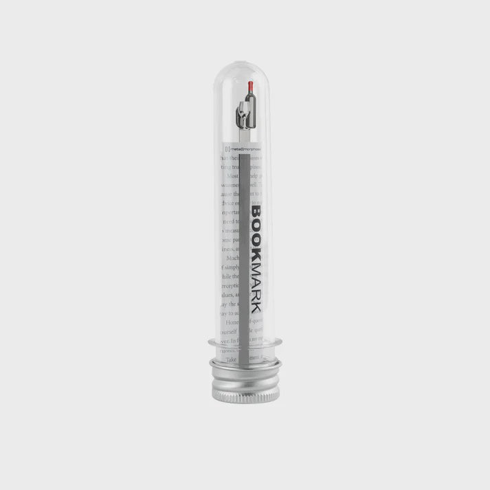 Clear cylindrical container with a wine bottle shaped metal bookmark inside.