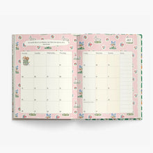An open planner or weekly calendar with pink striped and floral bunny-themed pages, photographed on a clean white background.